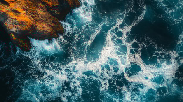 The ocean is rough and choppy, with white foam and bubbles. The water is a deep blue color, and the waves are crashing against the rocks. The scene is dynamic and full of energy, with the water photo