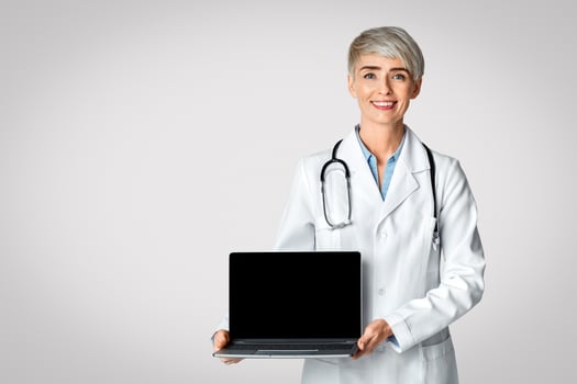 Online doctor concept. Smiling female in white coat shows a laptop with a blank screen. photo
