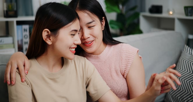 Portrait of Asian lesbian couple sitting on sofa happily admiring their engagement rings in a romantic atmosphere in a cozy room at home. LGBTQ Lifestyle. photo