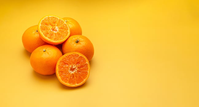 Pile of fresh oranges whole and half fruit on a yellow background with copy space for text photo
