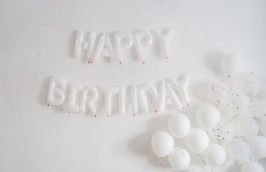 White Happy Birthday balloons on plain wall. Festive celebration concept photo