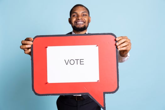 Hotel concierge holding a speech bubble with the message to vote, urging people to get interested in politics on camera. Skilled bellhop with suit and tie showing a marketing ad icon. photo