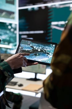 Male IT specialist explaining gps tracking to soldier by using a tablet connected to the satellite world map, military general headquarters. Telecommunications team provides air support. Close up. photo