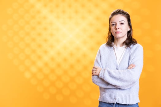 Portrait of woman crossing arms while posing, isolated over yellow studio background. Caucasian lady dressed in casual attire standing, looking at camera, feeling confident photo