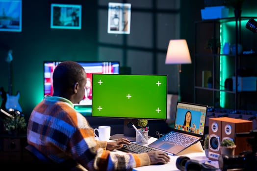 African american photo designer retouching images next to green screen on dual screens in a tech driven environment, representing modern digital media. Male graphic artist uses software tools.