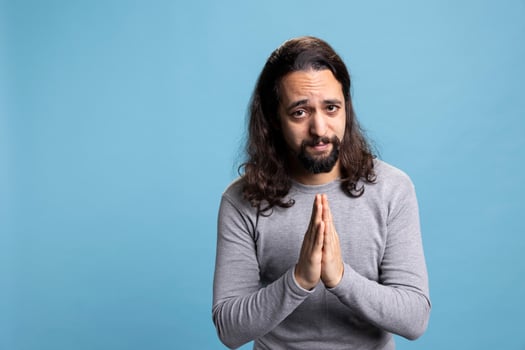 Spiritual guy praying to God and asking for forgiveness in studio, holding hands in a prayer and worshiping Jesus. Hopeful person with belief in Christianity and religious meditation on camera. photo