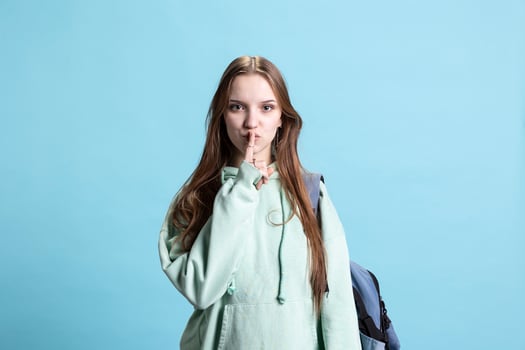 Stern woman doing shushing hand gesturing, irritated by noise, having negative mood. Girl placing finger on lips, doing quiet sign gesture, isolated over studio background photo