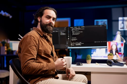 Portrait of cheerful computer engineer enjoying hot beverage while implementing security measures to protect company systems and data. Smiling IT worker drinking coffee and debugging code photo