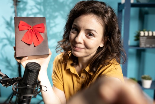 Joyful content creator holding present box, excited to do giveaway for subscribers, filming with selfie camera. POV shot of media star happy to offer packed gift with ribbon to viewers photo