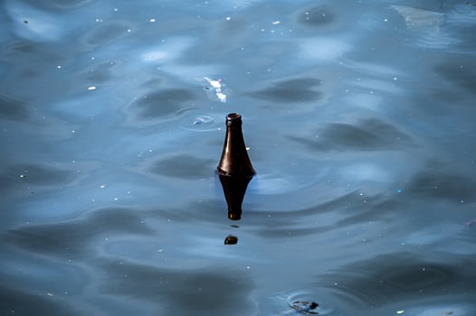 Used glass bottle floating in dirty river photo
