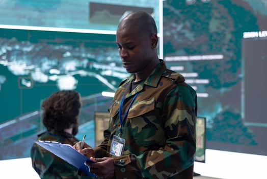 Army division officer overseeing special operation to gather real time information in control room with CCTV surveillance radar footage on a big screen. Soldier and crew targeting enemy power base. photo