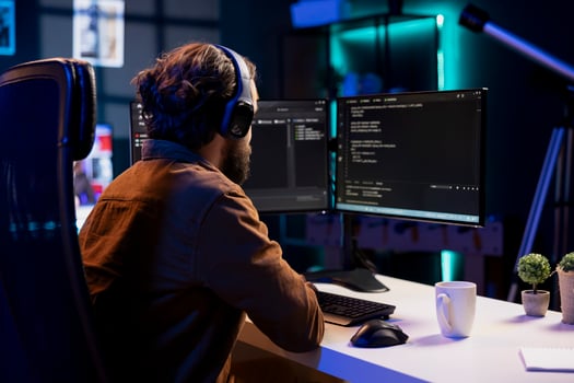 Man listening music while doing software quality assurance, reading source code on computer screen. Developer wearing headphones enjoying podcasts and inspecting coding on desktop PC photo
