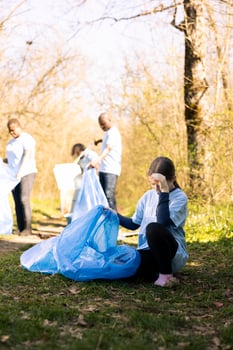Environmental volunteer girl gathering junk and plastic litter in a bag, recycling garbage in a disposal and cleaning the forest. Young child supporting ecology and zero waste activism. photo