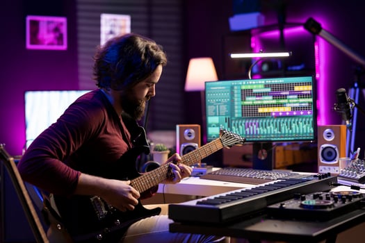 Young artist recording himself playing acoustic guitar in home studio, creating new string accords and editing them on daw software. Musician producing new soundtracks with instrument and amplifier. photo