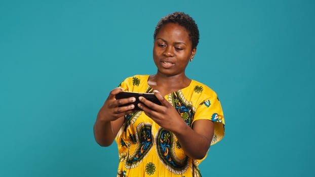 Cheerful woman gamer playing mobile videogames in studio, having fun with modern leisure activity on her smartphone app. Smiling person enjoys online gaming tournament online. Camera A. photo