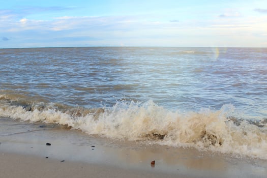Gentle Waves on a Calm Sea. Gentle waves lapping a sandy beach under a partly cloudy sky. photo