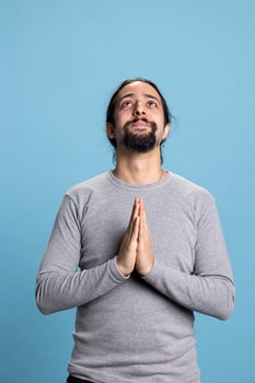 Male person posing with his hands in a prayer and worshipping God on camera, talking to Jesus Christ and showing belief in Christianity. Young adult being hopeful and meditating in studio. photo