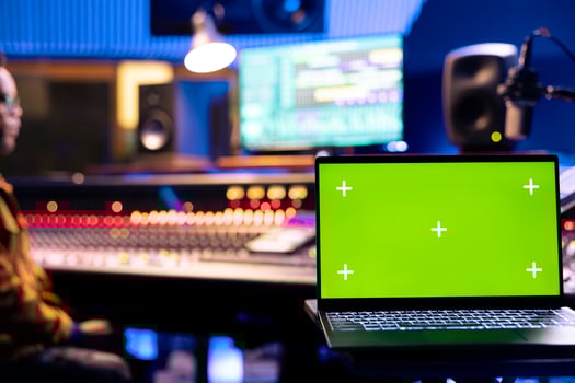 Focused audio engineer recording tracks on control panel board next to laptop with greenscreen, adjusting volume levels on mixing console. Sound designer creating music for his new album. photo
