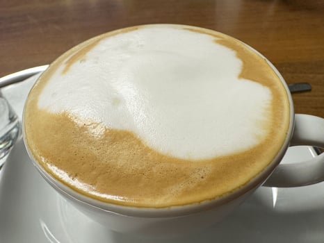 Creamy cappuccino coffee with foam in a white cup on a wooden table photo