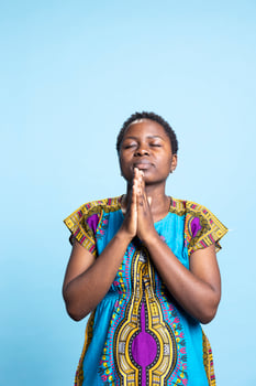 African american adult talking to Jesus Christ by saying grace, religious woman with belief praying to the Lord against blue background. Spiritual optimistic girl saying a prayer. photo