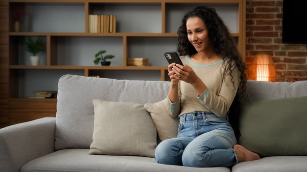 Adult woman lady using phone for bet in internet receive message with good news offer sitting on couch at home win mobile phone win game online victory virtual app success winning triumph celebrate photo