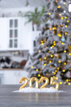 Golden number 2025 on table in background of cozy white kitchen with Christmas tree and Christmas decor with garland lights. Housing, interior, renovation, mortgage, rent in New Year photo
