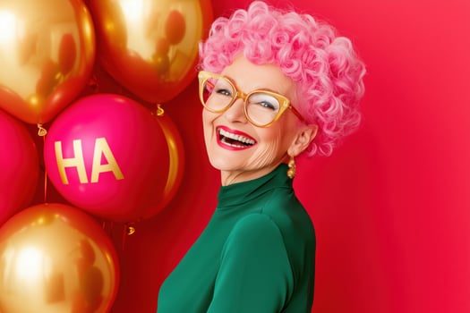 Cheerful grandmother with vibrant pink hair and oversized glasses celebrates happiness with golden balloons on a bright red background photo