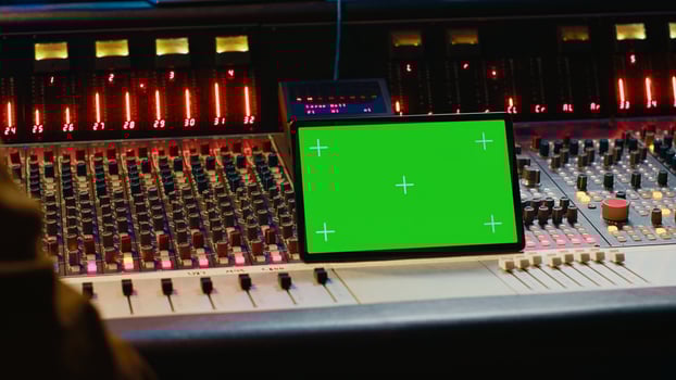 Music producer holding a tablet with greenscreen display on mixing console in control room, twisting knobs and pushing faders to edit audio recordings. Processing sounds. Camera A. photo