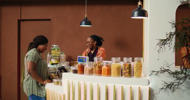 Local vendor putting merchandise on scale at checkout, ensuring the best pricing value for regular client at grocery store. African american retailer serving buyer, eco friendly. Handheld shot. photo