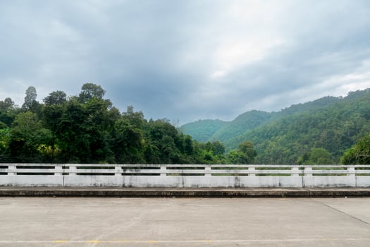 Horizontal or Landscape view of a concrete road. Side of concrete bridge fence. Background of green forest and mountain under sky. At Mae Ngao Mae Hong Son of Thailand. photo