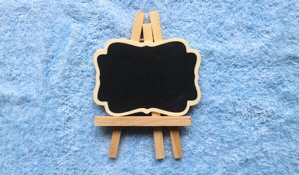Wooden easel mini blackboard with faded chalk surface, isolated on blue background. Blank space for text photo