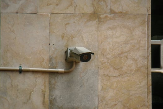 A security camera mounted on a beige marble wall, connected by a conduit cable, symbolizing surveillance, safety, and modern security systems. photo