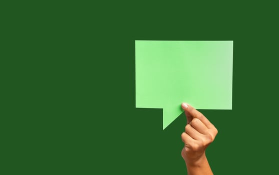 Close-up of hand holding a green speech bubble against a green background photo