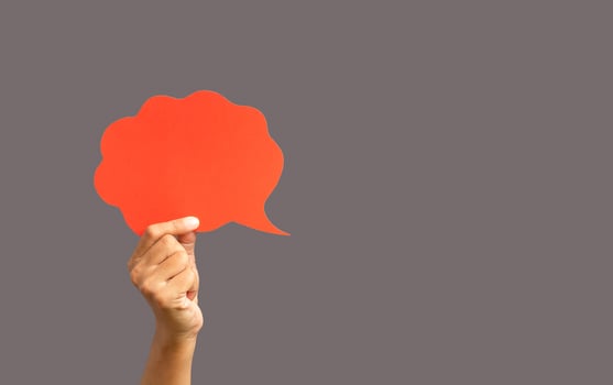 Close-up of hand holding a red speech bubble against a gray background photo
