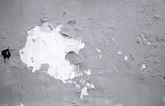 Close-up of a weathered wall showing peeling paint, cracks, and rough texture in a monochromatic tone. photo