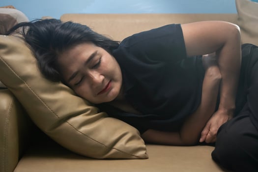 Women wearing shirt black suffering from severe stomach ache while lying on sofa in the living room, feeling extremely sick, healthy care concept photo