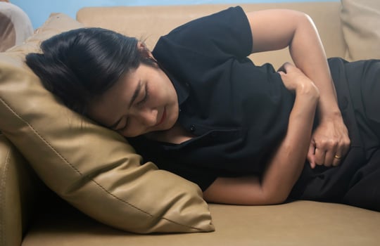 Women wearing shirt black suffering from severe stomach ache while lying on sofa in the living room, feeling extremely sick, healthy care concept photo