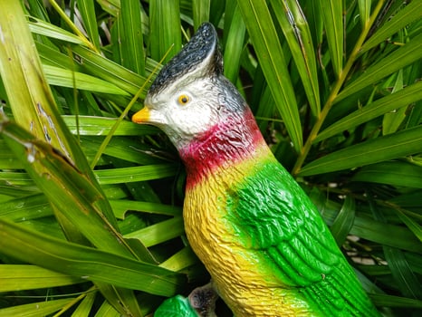 statue of a parrot animal character on a twig on a leaf background photo