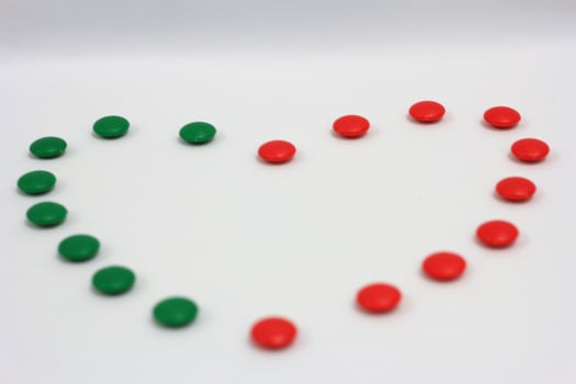 Heart shape made of green and red circular candies on a clean white background, symbolizing love, harmony, and festive themes photo
