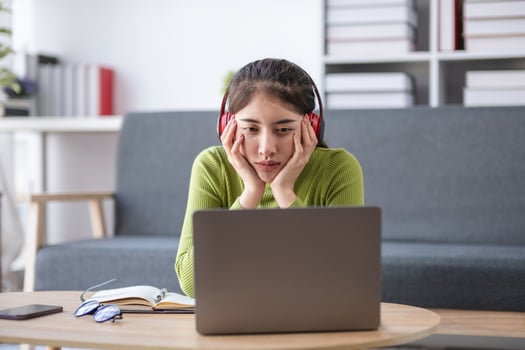 Asian woman feeling stressed while working on laptop with headphones in modern office, concept of stress photo
