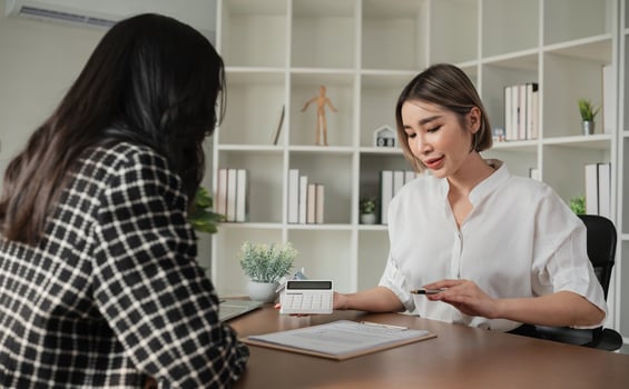 Two Asian businesswomen discussing financial documents with calculator at office desk. Concept of business finance and professional consultation photo