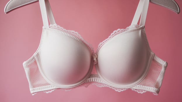 Elegant white lace bra suspended against a soft pink background, highlighting its delicate design. photo