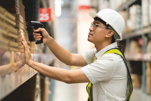 A man in a white shirt and yellow vest is standing in a warehouse, holding a barcode scanner photo