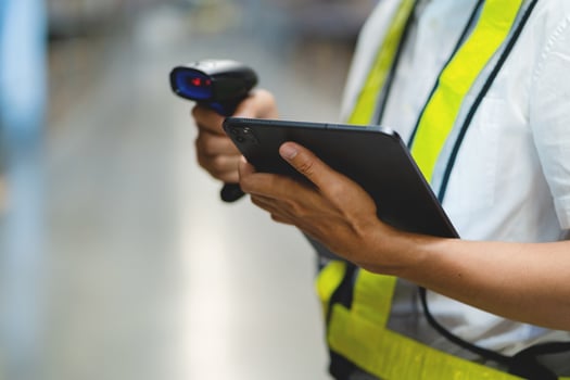 A person in a yellow safety vest is holding a tablet and a barcode scanner. They are likely working in a warehouse or a similar setting where they need to scan items for inventory or tracking purposes photo