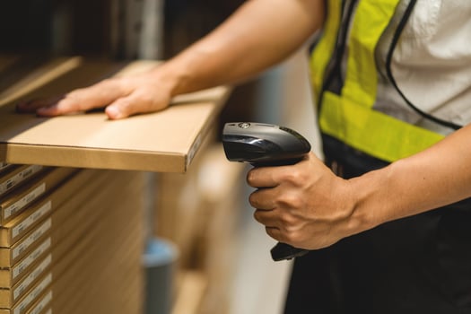 A person is using a barcode scanner in a warehouse. The person is wearing a yellow vest and black pants photo