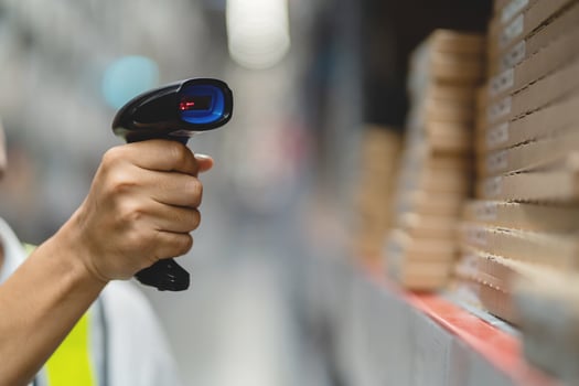 A person is holding a barcode scanner in a warehouse. The person is wearing a yellow vest photo