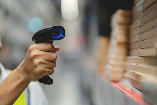 A person is holding a barcode scanner in a warehouse. The person is wearing a yellow vest photo