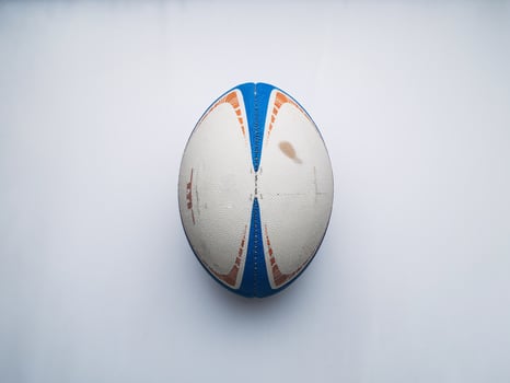 A worn rugby ball with blue and orange detailing, resting on a clean white surface. photo