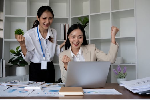Two Asian businesswomen celebrating success while working on a laptop in the office. Concept of achievement and teamwork photo