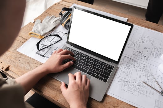 Engineering Team Collaborating on Work Plans with Laptop with white screen and Blueprints on Wooden Table photo